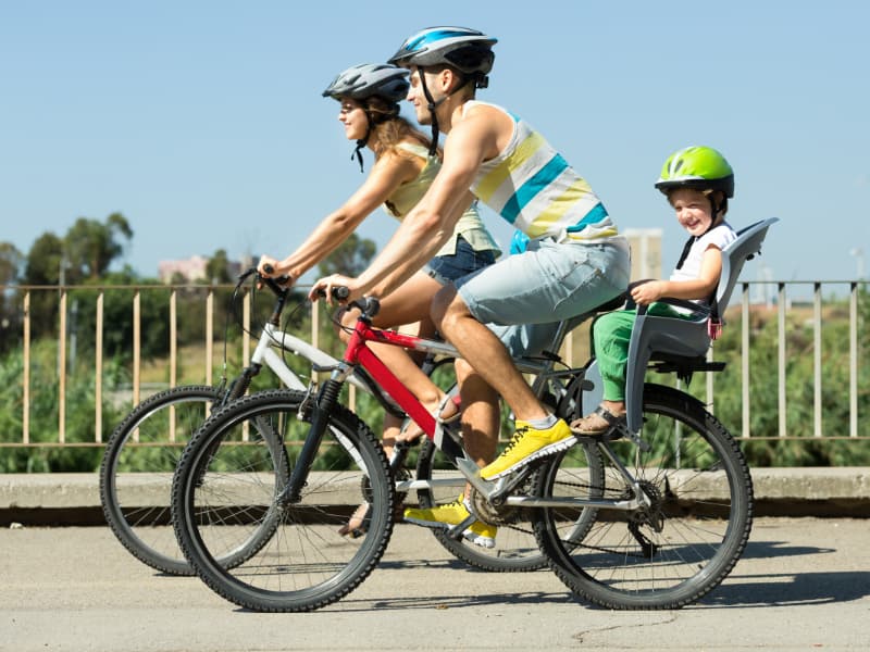 Parents riding bicycles, with a helmeted child riding behind in his seat