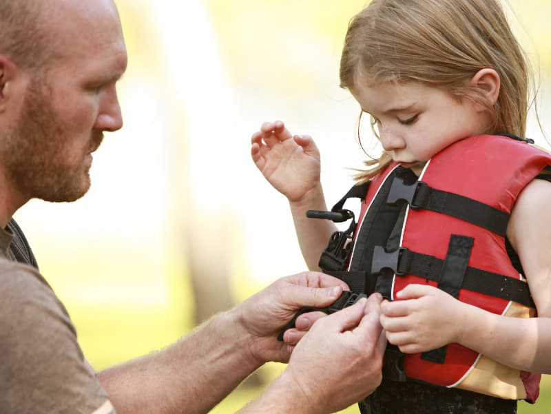 A father adjusts the fit of his daughter's safety vest