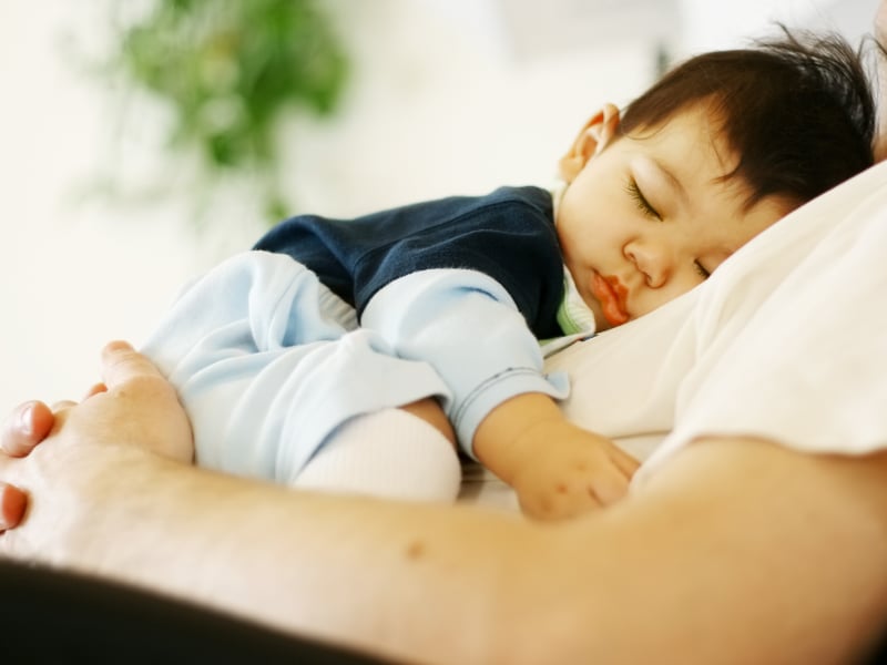 An infant asleep on their parent's chest